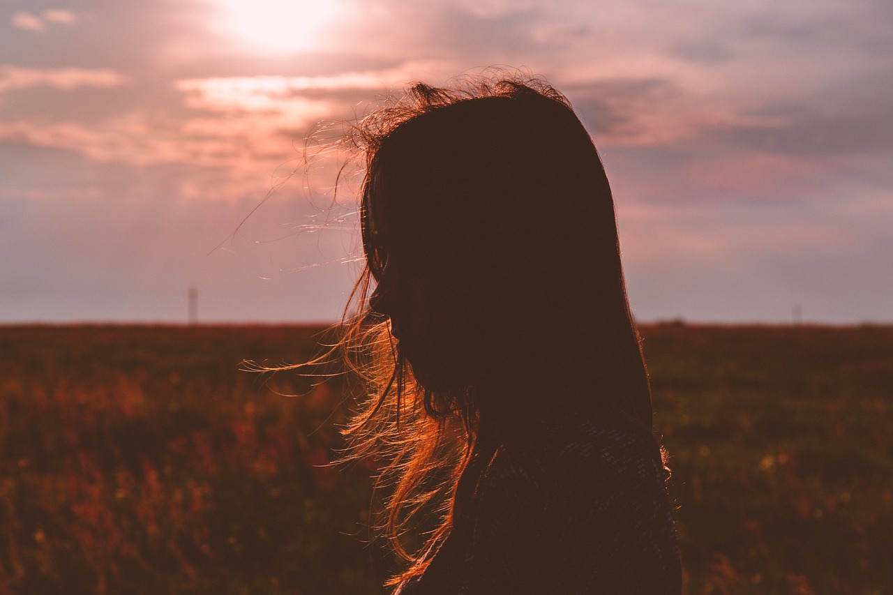 Writing is hard. Profile of woman in a field, with the sun behind her and her hair covering most of her face.